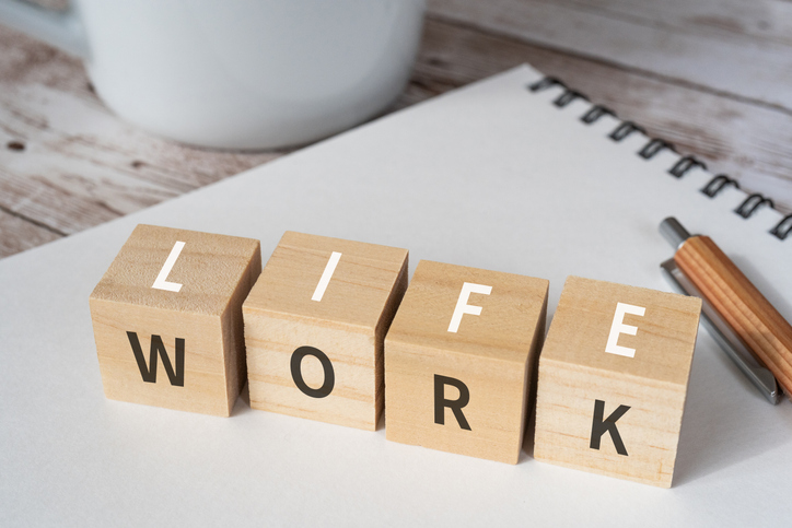 Wooden blocks with "LIFE" and "WORK" text displaying importance of work/life balance, a pen, a notebook, and a cup.