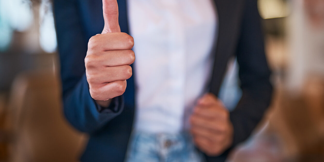 Thumbs up hand sign, symbol and gesture showing success, support and trust. Closeup finger or thumb of businesswoman endorsing idea, plan or strategy and expressing content and approval to good news